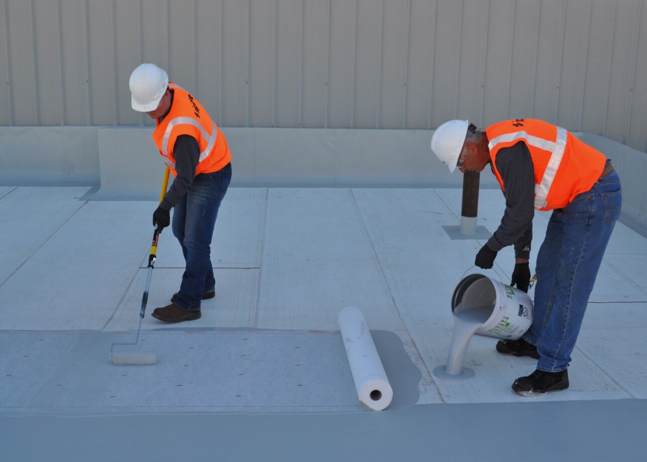 Two Siplast workers pouring and rolling pmma roof membrane