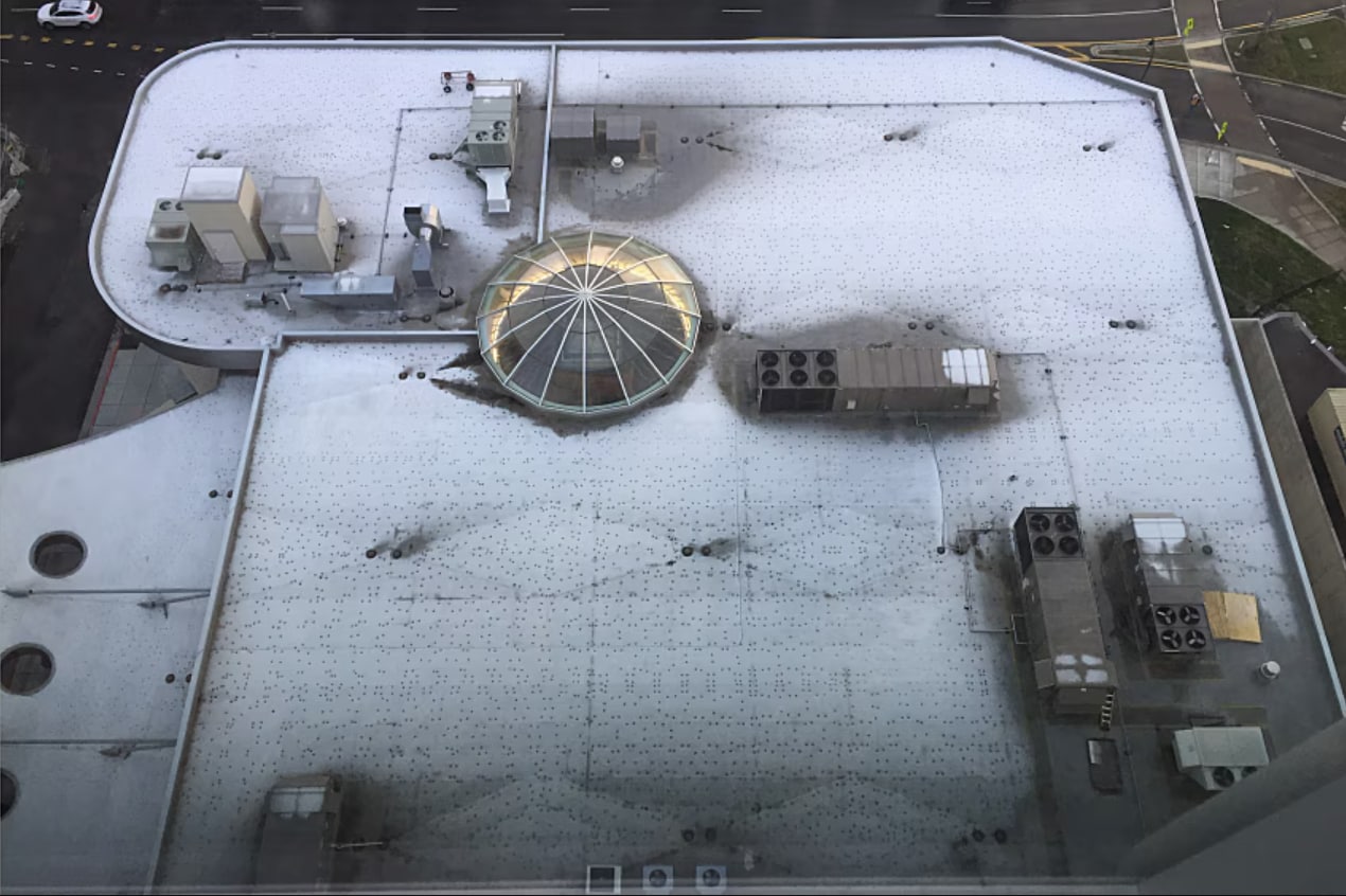 Aerial view of a flat roof with melted snow pattern of dots that are caused by the interior heat loss through the fasteners and plates.